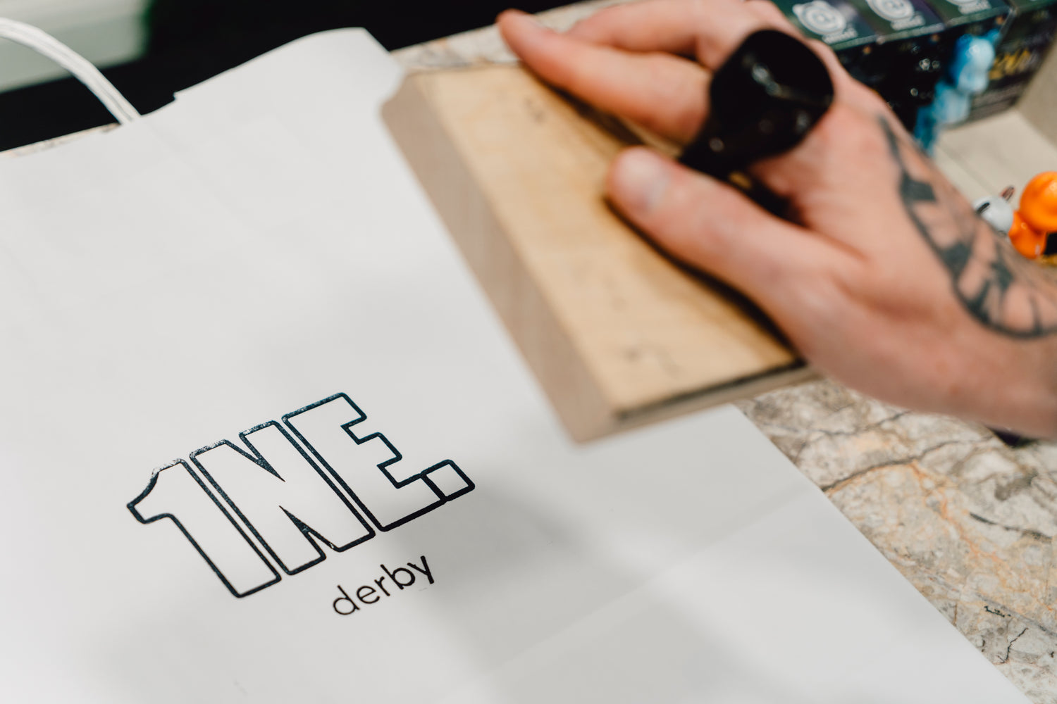 Person using a stamp on a paper  carrier bag with '1NE. derby' printed on it. 