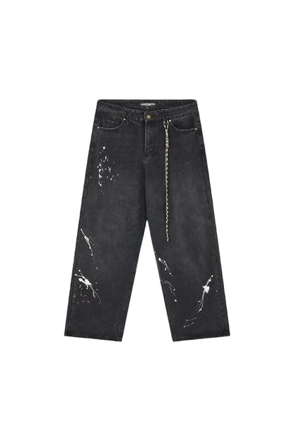 Black washed denim jeans with white paint splatter details and a decorative gold chain hanging from the side pocket, displayed flat against a light gray background.